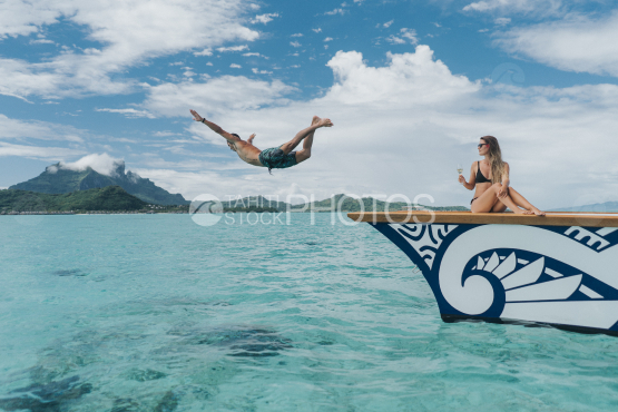 BORA BORA, couple of tourist on outrigger, the husband jumping in the lagoon